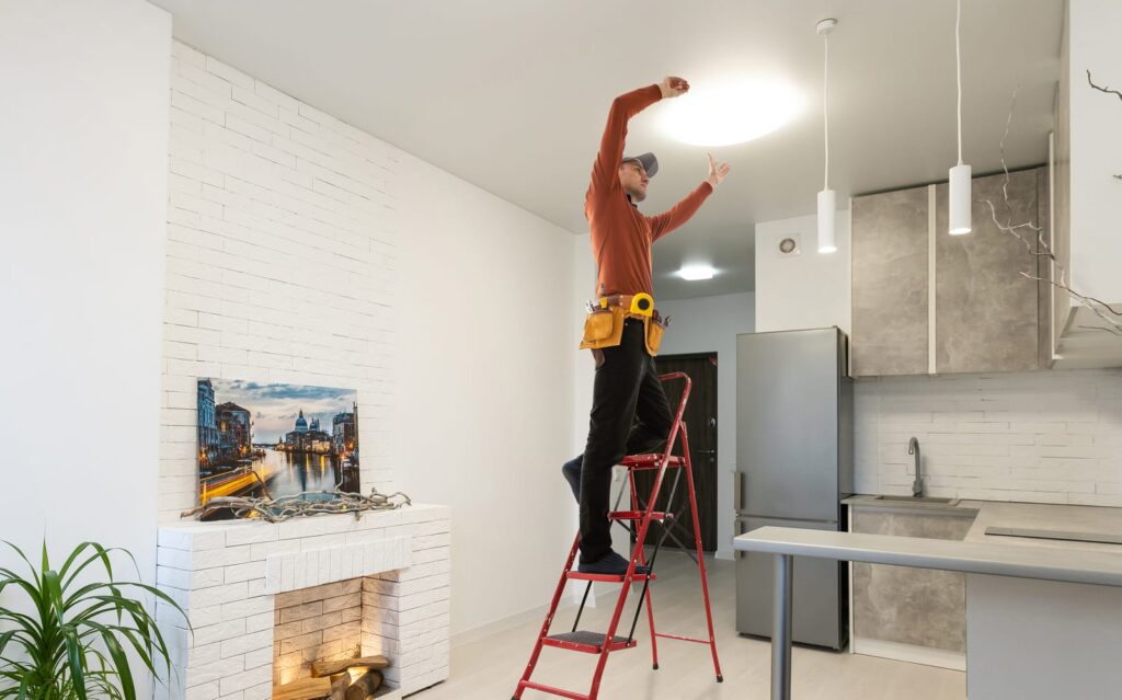 Man on a ladder installing smart lights into a home.