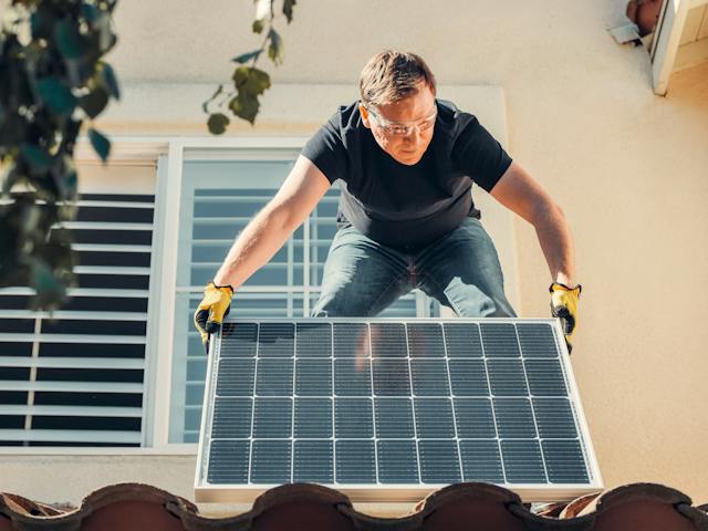 Man renovating a house to make it more sustainable by placing a solar panel on the roof. 